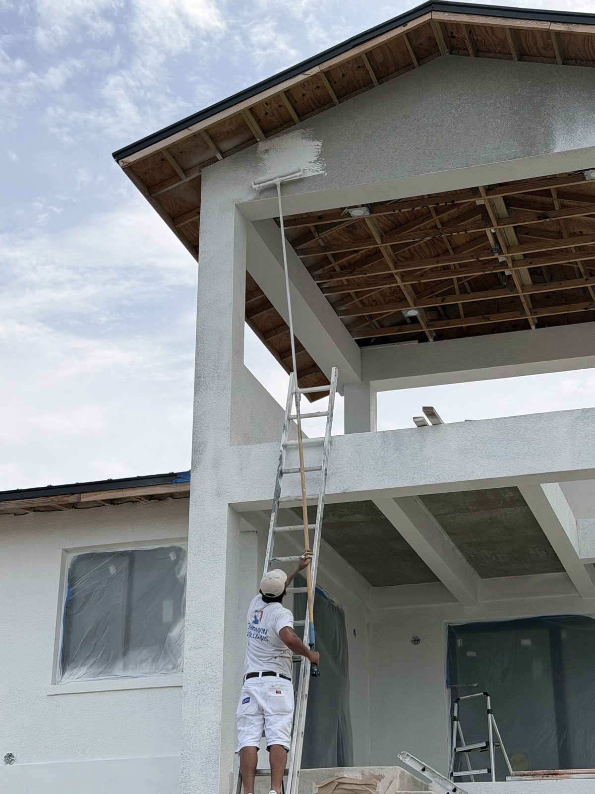 Painter on extension ladder finishing high eaves on a Tampa home